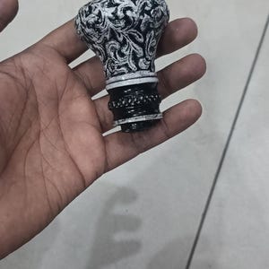 Puede incluir: Tapón de botella decorativo con un diseño floral en blanco y negro. El tapón tiene una parte superior redondeada y un patrón detallado. La base es negra con una banda decorativa plateada. Una adición única a cualquier colección de bar.