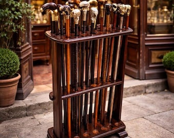 May include: A dark wooden display stand holding a collection of walking sticks with decorative handles. The handles are in gold, silver, and dark wood. The stand is on a stone surface, with a shop entrance visible in the background.
