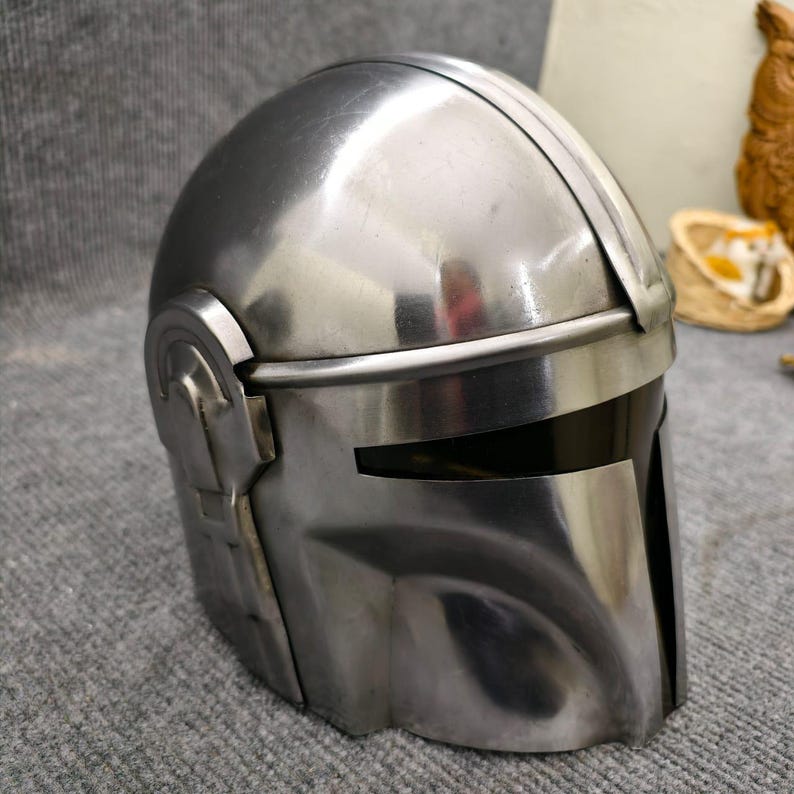 Puede incluir: Un casco plateado met&aacute;lico con visera y detalles en las orejas. El casco tiene una superficie lisa y reflectante y un dise&ntilde;o que recuerda a una est&eacute;tica espacial. El casco es probablemente un disfraz o un objeto de colecci&oacute;n.