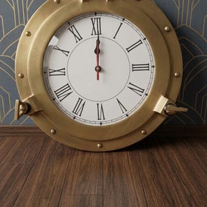 Reloj de pared de latón con forma de ojo de buey, decoración marinera steampunk con números romanos.