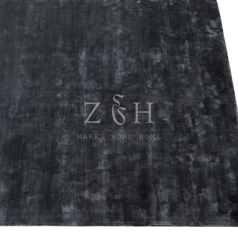 Puede incluir: Una alfombra gris oscuro con una superficie texturizada. La alfombra tiene un aspecto descolorido y presenta el texto "Z & H MAKES HOME HOME" en un color gris m&aacute;s claro.