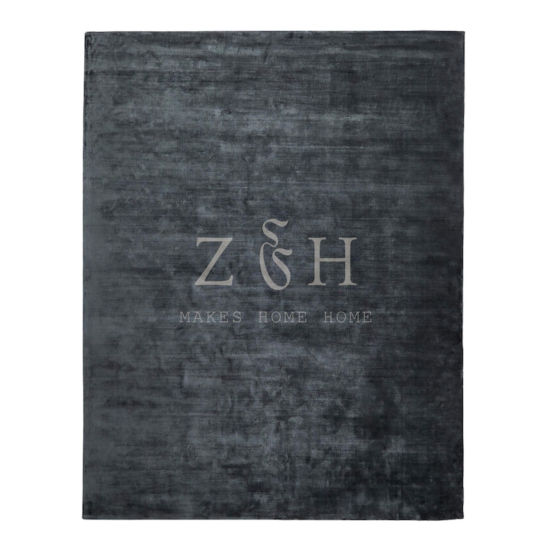 Puede incluir: Una alfombra rectangular gris oscuro con una superficie texturizada. La alfombra presenta el texto "Z & H MAKES HOME HOME" en una fuente gris m&aacute;s clara, centrada en la alfombra. La alfombra est&aacute; dise&ntilde;ada para la decoraci&oacute;n del hogar.