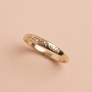 May include: A polished gold band ring featuring the engraved cursive text Till Death along the outer surface. The ring has a smooth, rounded profile and a reflective metallic finish, showcasing the detailed script lettering etched into the metal.