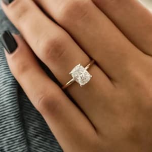 Puede incluir: Un anillo de oro con una gran gema clara de forma rectangular. El anillo está en un dedo, y la mano descansa sobre una pierna vestida con mezclilla. La banda del anillo es delgada y simple, complementando la prominente gema.