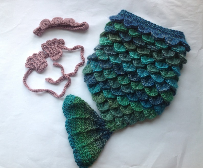 Puede incluir: Un disfraz de cola de sirena de ganchillo en tonos azules y verdes con una diadema y pu&ntilde;os a juego de color rosa.