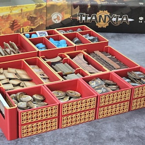 Könnte beinhalten: Roter Spiel-Organizer mit mehreren Fächern, die Spielsteine enthalten. Der Organizer hat ein dekoratives goldenes Gittermuster auf der Vorderseite der Schubladen. Die Spielbox im Hintergrund ist mit "Tianxia" beschriftet.