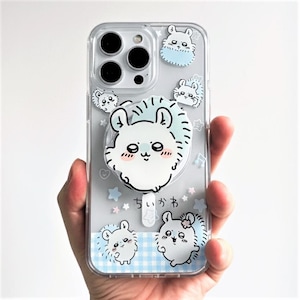 May include: Clear phone case with a cute cartoon hedgehog design. The case features a pop socket with a large hedgehog face and smaller hedgehog illustrations. The background includes stars, musical notes, and Japanese text.