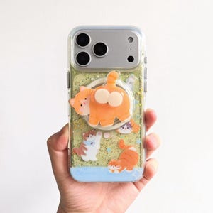 May include: Clear phone case with a glittery green background and several cartoon cat designs. The cats are orange, white, and calico. The case has a clear border and a blue base with the word "Cat" printed on it.