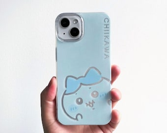 May include: A light blue smartphone case featuring a cartoon character with a blue bow and the text CHIIKAWA printed vertically along the right side. The case has a clear cutout for the dual camera lens system on the upper left corner.