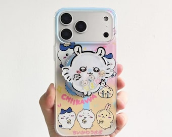 May include: A clear smartphone case featuring a colorful Chiikawa character print with a matching circular phone grip. The design includes various small cartoon figures, the text CHIIKAWA, and Japanese characters, set against a gradient background.