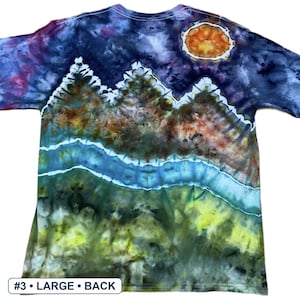 May include: A short-sleeve t-shirt featuring a tie-dye landscape design with a dark blue and purple night sky, a bright orange sun, jagged mountain peaks, a flowing blue river, and a green grassy foreground. The text #3 &bull; LARGE &bull; BACK is visible.
