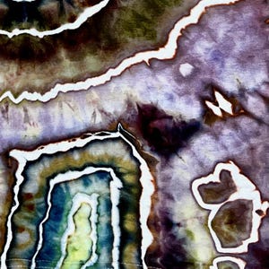 May include: A fabric surface featuring a tie-dye pattern with organic, geode-like shapes in shades of deep purple, muted olive green, and dark blue. The design is defined by sharp, irregular white lines that separate the various color zones.