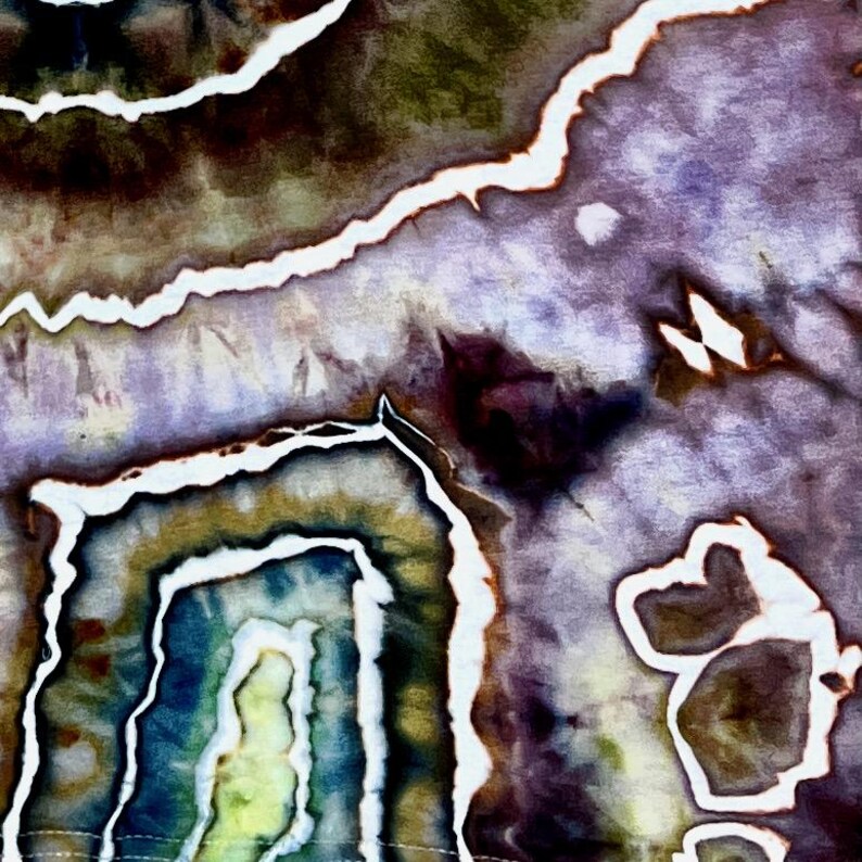 May include: A fabric surface featuring a tie-dye pattern with organic, geode-like shapes in shades of deep purple, muted olive green, and dark blue. The design is defined by sharp, irregular white lines that separate the various color zones.