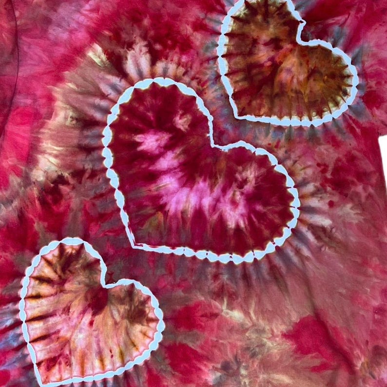 Może przedstawiać: Odzież z tkaniny z wzorem tie-dye w odcieniach głębokiej czerwieni, magenty i brązu. Wz&oacute;r zawiera trzy wyraźne motywy w kształcie serca, z kt&oacute;rych każdy jest obwiedziony wyraźną białą linią kontrastującą z tłem o mieszanych kolorach.