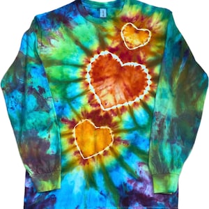 Może przedstawiać: Koszulka z długim rękawem i okrągłym dekoltem z żywym wzorem tie-dye w odcieniach niebieskiego, zielonego, ż&oacute;łtego i pomarańczowego. Z przodu znajdują się trzy wyraźne kształty serc o r&oacute;żnych rozmiarach, każde z białą obw&oacute;dką na tle wzoru.