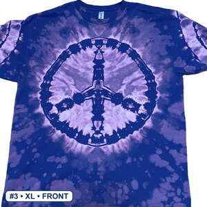 Peut inclure: Un t-shirt &agrave; manches courtes avec un motif tie-dye dans des tons bleu fonc&eacute; et violet clair. Le centre du t-shirt pr&eacute;sente un grand signe de paix circulaire dans un ton bleu plus fonc&eacute;. Une &eacute;tiquette blanche en bas indique #3 &bull; XL &bull; FRONT.