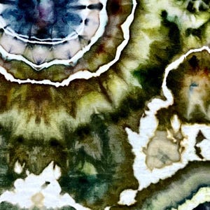 May include: A textile fabric featuring a tie-dye pattern with concentric circular shapes in shades of deep forest green, olive, and dark navy blue. The design includes distinct white lines that separate the color gradients, creating a high-contrast, organic, and fluid appearance across the surface of the material.
