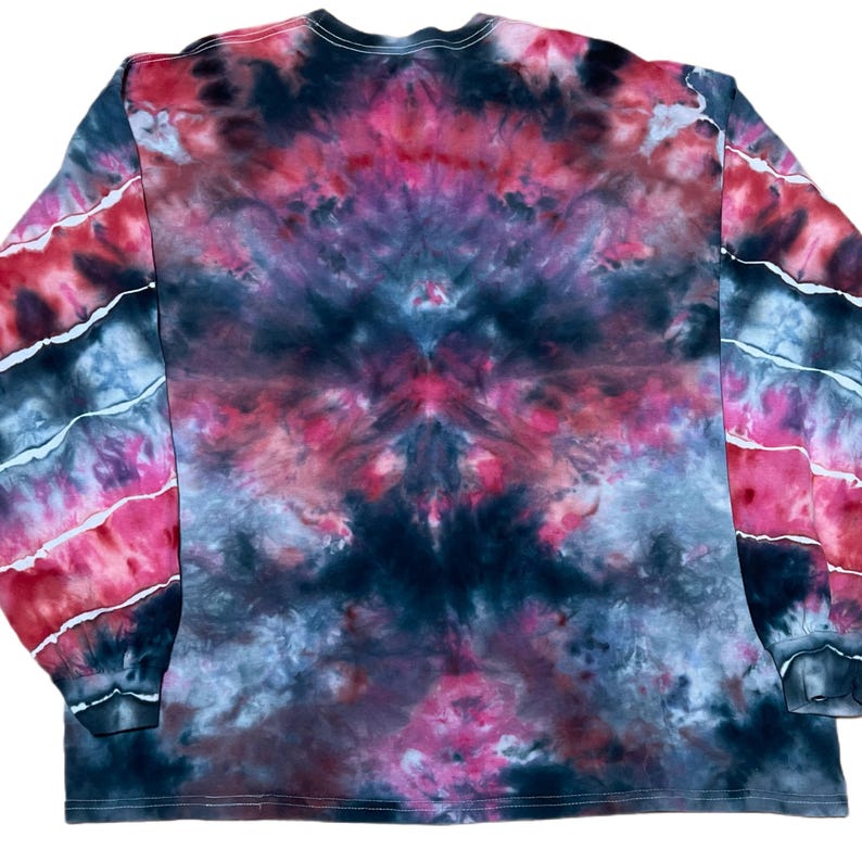 May include: A long-sleeve shirt featuring a tie-dye pattern in shades of black, dark gray, and vibrant pink. The design displays a symmetrical, cloud-like distribution of colors across the torso, while the sleeves show diagonal stripes.