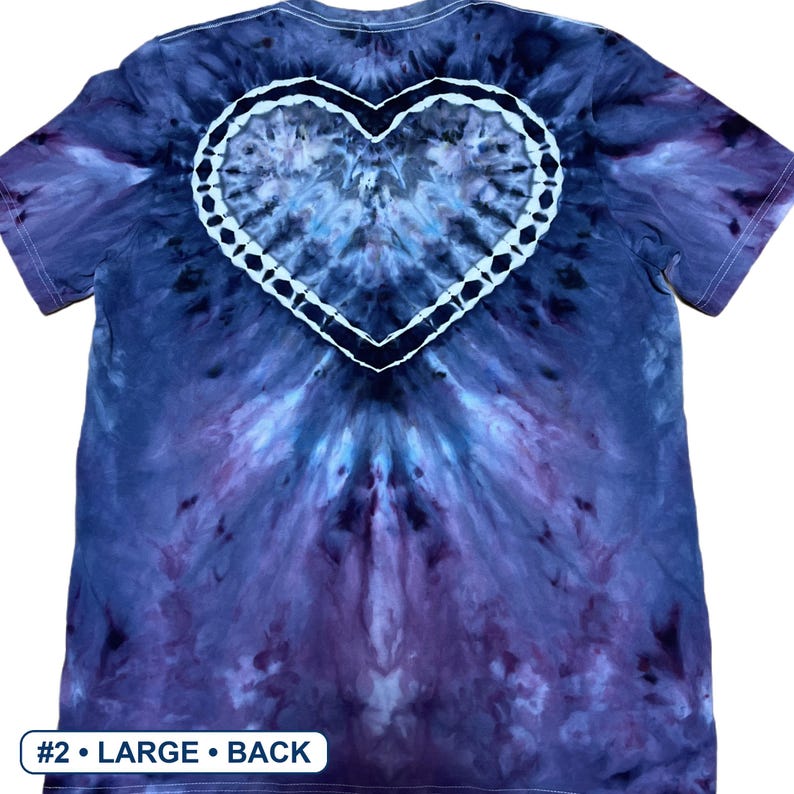 Może przedstawiać: Koszulka z kr&oacute;tkim rękawem z wzorem tie-dye w odcieniach ciemnego błękitu, fioletu i czerni. Na plecach wyśrodkowano wyraźny biały kształt serca, obwiedziony ciemną ramką. Mała biała etykieta na dole zawiera napis #2 &bull; LARGE &bull; BACK.