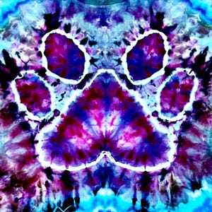 Op de afbeelding: Een tie-dye ontwerp met een grote pootafdruk in paars, roze en blauw. De pootafdruk is wit omlijnd tegen een wervelende achtergrond van vergelijkbare kleuren. Het algehele effect is een levendig, psychedelisch patroon.