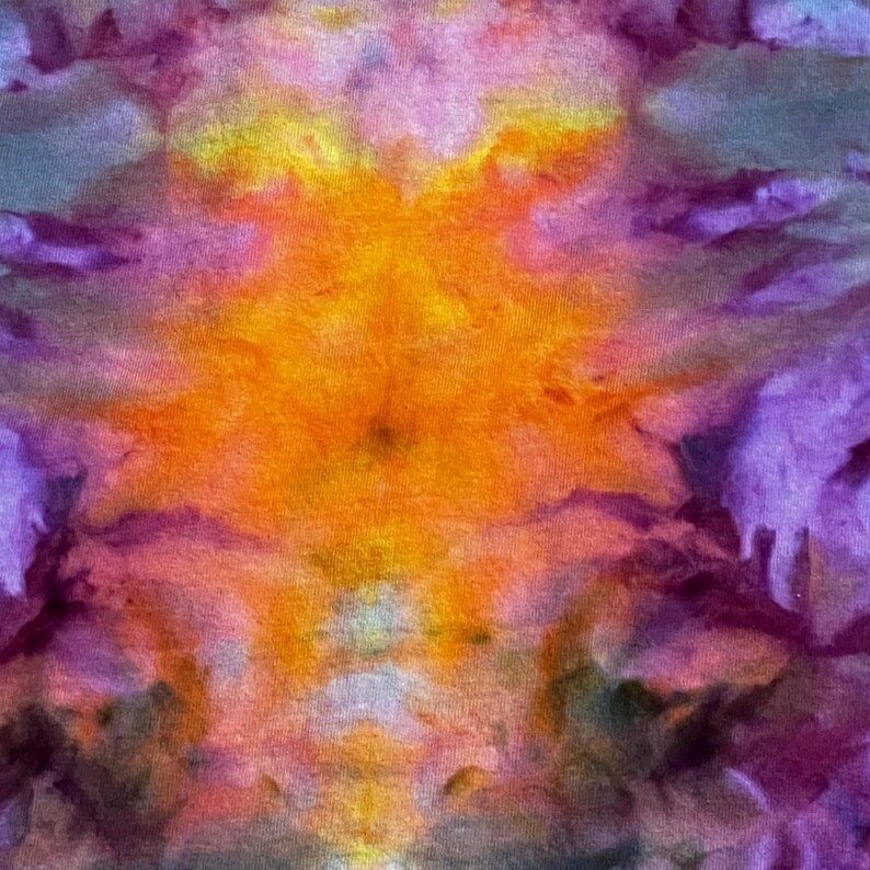 May include: A fabric surface featuring a tie-dye pattern with a vibrant central burst of bright yellow and orange, transitioning into soft pinks and deep purple hues toward the edges, creating a blended, cloud-like abstract color effect.