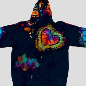 May include: A black long-sleeve hooded sweatshirt featuring a vibrant, multi-colored tie-dye heart graphic on the chest. The hoodie includes additional tie-dye patterns in shades of blue, purple, orange, and green on the hood and sleeves.