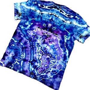 以下が含まれることがあります： 青、紫、白の色合いのタイダイTシャツ。シャツは、中央に紫色のエリアと白いアクセントがある渦巻き模様が特徴です。半袖シャツは柔らかい素材で作られています。