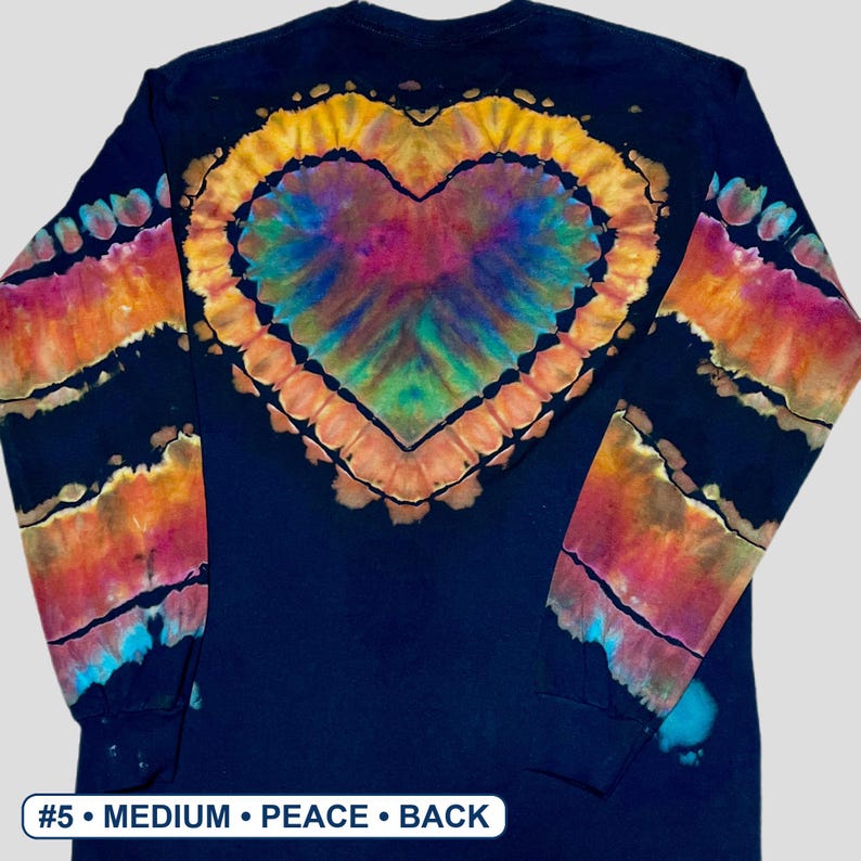 May include: A long-sleeve black shirt featuring a large, central tie-dye heart pattern in shades of yellow, orange, pink, purple, and blue. The sleeves have matching tie-dye stripes. A white label at the bottom reads #5 &bull; MEDIUM &bull; PEACE &bull; BACK.