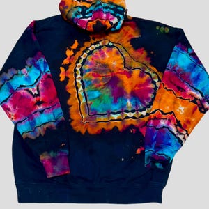 May include: A black hoodie featuring a vibrant tie-dye heart design on the back. The heart is outlined in a repeating pattern and filled with bright orange, pink, purple, and blue colors. The sleeves and hood also display matching tie-dye patterns.