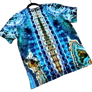 May include: A short-sleeved tie-dye t-shirt in shades of blue, teal, and brown. The shirt features a central vertical pattern with white and brown accents, and a swirling design on the sleeves.