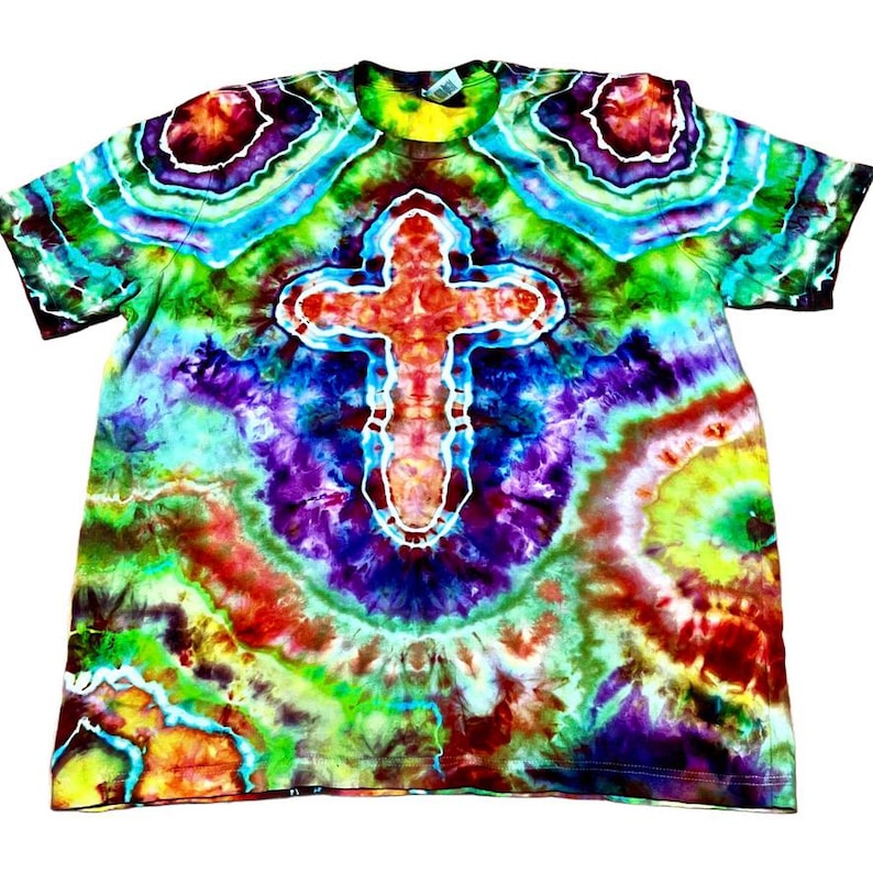 Może przedstawiać: Kolorowa koszulka typu tie-dye z dużym wzorem krzyża pośrodku. Koszulka charakteryzuje się żywą mieszanką kolor&oacute;w, w tym czerwonym, pomarańczowym, ż&oacute;łtym, zielonym, niebieskim i fioletowym. Krzyż jest obrysowany na biało.