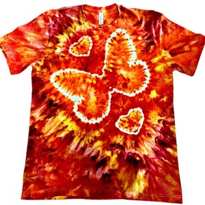 May include: A tie-dye t-shirt in shades of red, orange, and yellow, with a heart-shaped design outlined in white. The shirt has short sleeves and a crew neck, with a vibrant, swirling pattern throughout.