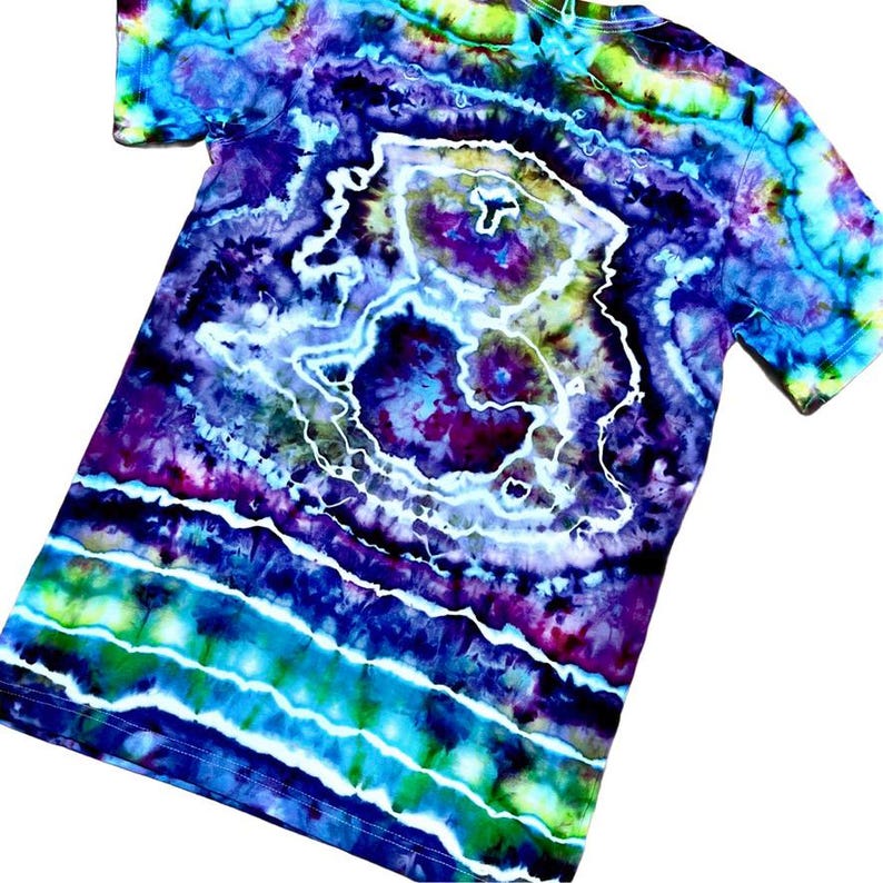 May include: A tie-dye t-shirt with a vibrant, swirling pattern in shades of blue, purple, green, and white. The design features concentric circles and wavy lines, creating a psychedelic effect. The shirt has short sleeves and a crew neck.