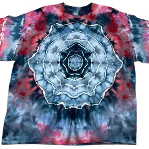 May include: A short-sleeve t-shirt featuring a tie-dye pattern with a central circular mandala-like design in shades of black, gray, and white, surrounded by a vibrant outer border of deep red, pink, and dark charcoal tones throughout the fabric.