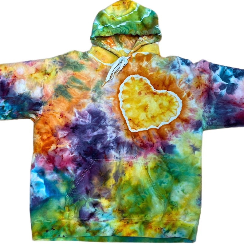 May include: A long-sleeve hooded sweatshirt featuring a vibrant tie-dye pattern in shades of yellow, orange, purple, blue, and green. The front displays a prominent, white-outlined yellow heart shape, and the hood includes white drawstrings.