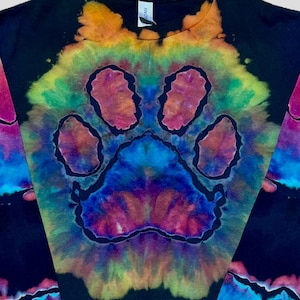 May include: A black long-sleeve t-shirt featuring a large, central tie-dye paw print design. The graphic displays vibrant, blended colors including orange, yellow, green, blue, and magenta, set against the dark fabric background.