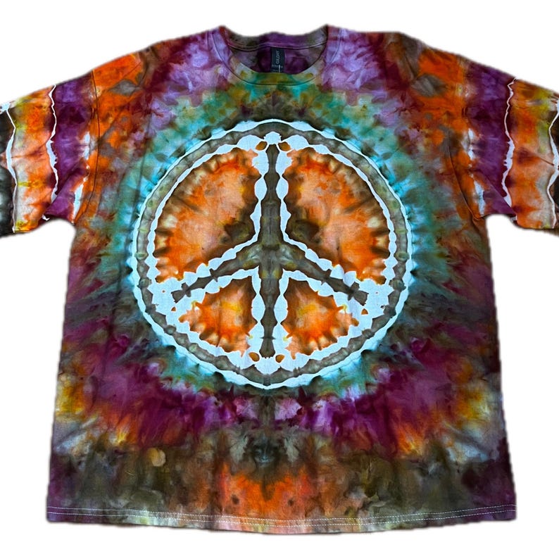 May include: A short-sleeve crew neck t-shirt featuring a tie-dye pattern in shades of orange, purple, brown, and teal. A large, white, circular peace sign graphic is centered on the front, surrounded by a radiating tie-dye design.