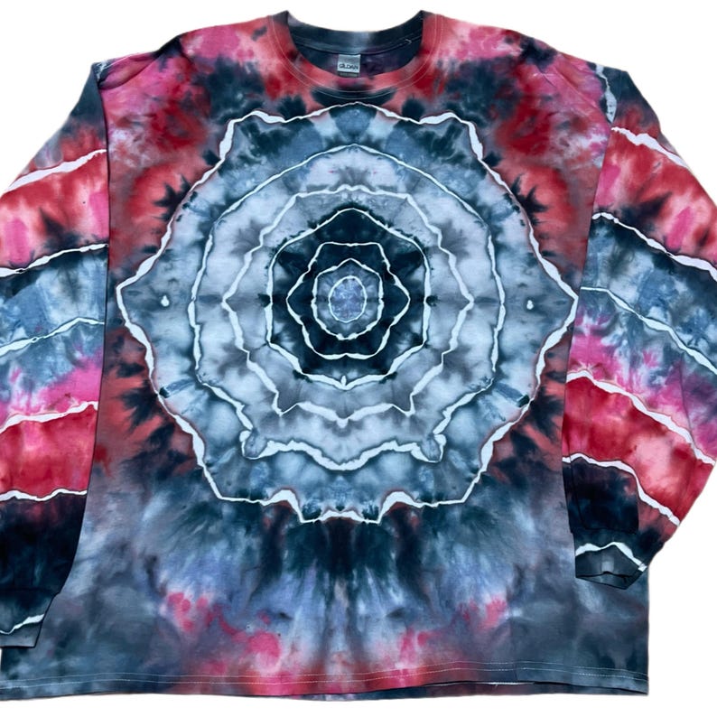 May include: A long-sleeve crew neck shirt featuring a tie-dye pattern with a large, central circular mandala-like design in shades of black, gray, and white, surrounded by vibrant red and pink accents that extend across the sleeves and body.