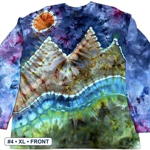 May include: A long-sleeve tie-dye shirt featuring a landscape design with a dark blue sky, a bright orange sun, brown mountain peaks, and a green grassy foreground. The text #4 &bull; XL &bull; FRONT is printed in a white box at the bottom left corner.