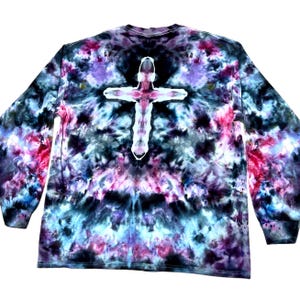 May include: A long-sleeve shirt featuring a tie-dye pattern in shades of black, purple, blue, and pink. The center of the garment displays a prominent white cross shape created through the tie-dye process, set against the dark, mottled background.