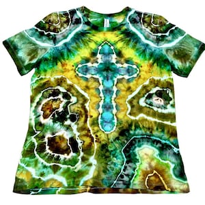 Puede incluir: Una camiseta de manga corta te&ntilde;ida con tinte en tonos verdes, amarillos y azules. La camiseta presenta un dise&ntilde;o de cruz central y un patr&oacute;n abstracto. La tela parece suave y c&oacute;moda.