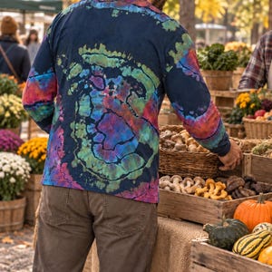May include: A long-sleeve shirt featuring a dark navy blue base with a vibrant tie-dye spiral pattern in shades of green, purple, and red. The shirt has a crew neckline and long sleeves, showcasing a colorful, swirling design across the back.