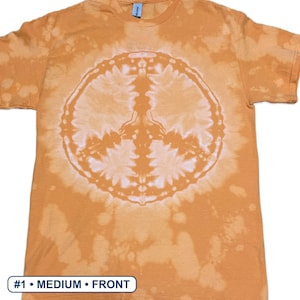 Peut inclure: Un t-shirt &agrave; manches courtes et col rond de couleur orange sourd avec un effet tie-dye d&eacute;color&eacute;. Un grand motif circulaire blanc repr&eacute;sentant un signe de paix est centr&eacute; sur le devant du v&ecirc;tement. Le texte #1 &bull; MEDIUM &bull; FRONT est visible en bas.