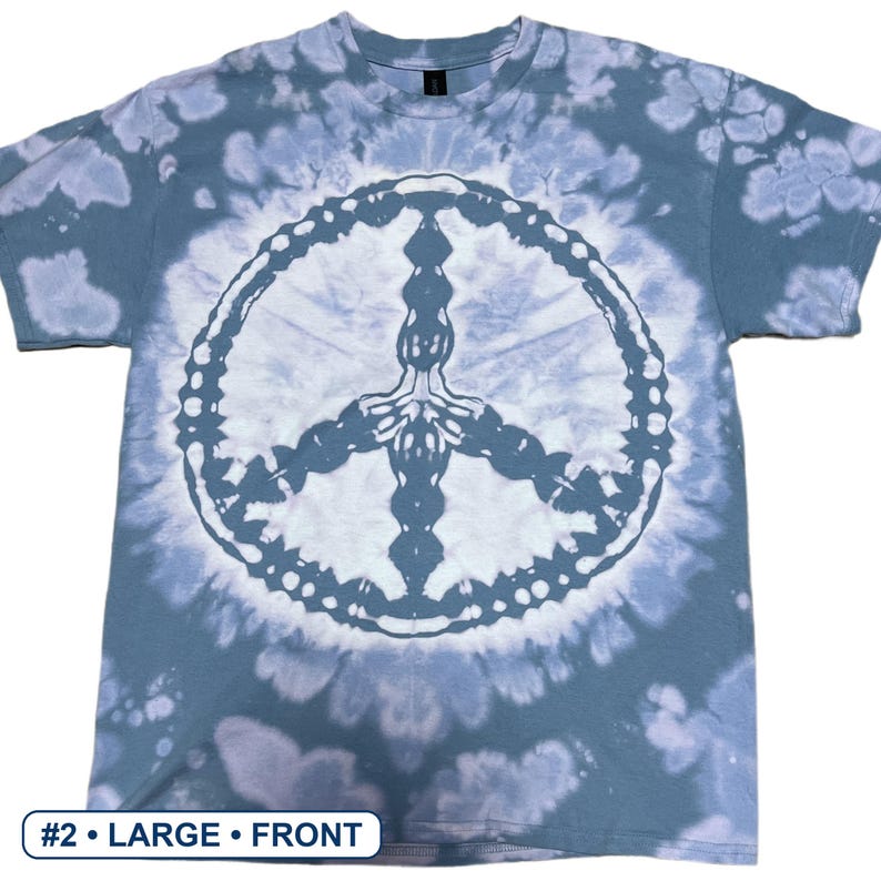 Peut inclure: Un t-shirt &agrave; manches courtes pr&eacute;sentant un motif tie-dye bleu et blanc avec un grand signe de paix blanc au centre. Le t-shirt comporte une petite &eacute;tiquette rectangulaire dans le coin inf&eacute;rieur gauche avec le texte #2 &bull; LARGE &bull; FRONT.