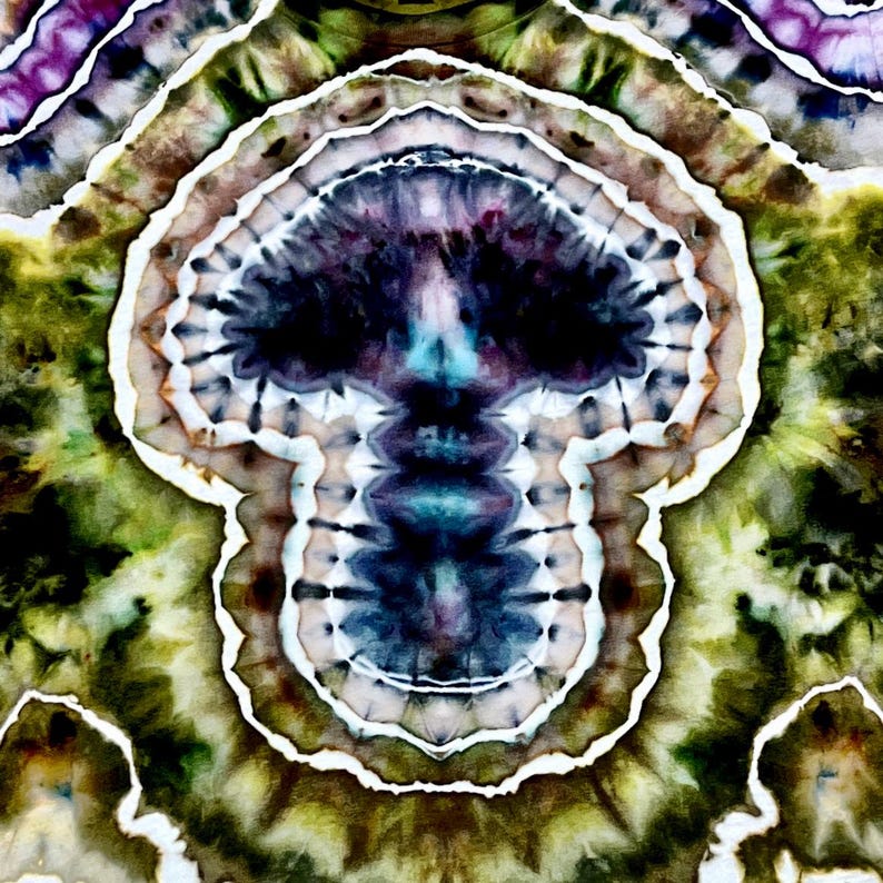 May include: A tie-dye fabric featuring a central skull-shaped motif in shades of deep purple, dark blue, and black, surrounded by concentric rings of white, olive green, and brown, creating a symmetrical, layered, and highly detailed pattern.