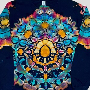 May include: A long-sleeve shirt featuring a black base with a vibrant, symmetrical tie-dye pattern centered on the chest. The design consists of intricate, repeating geometric shapes in shades of bright yellow, orange, turquoise, and magenta.