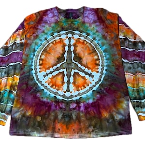 May include: A long-sleeve tie-dye shirt featuring a large, central white peace sign graphic. The fabric displays a vibrant, swirling pattern of orange, purple, teal, and brown hues. The sleeves are decorated with horizontal, wavy bands of color.