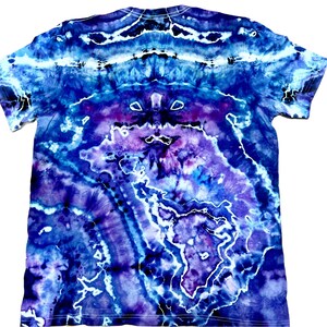 以下が含まれることがあります： 青、紫、白の色合いの鮮やかなタイダイ模様の半袖Tシャツ。 デザインは渦巻くパターンと対称的なレイアウトが特徴で、ユニークで芸術的な外観を作り出しています。 シャツは柔らかい素材で作られています。