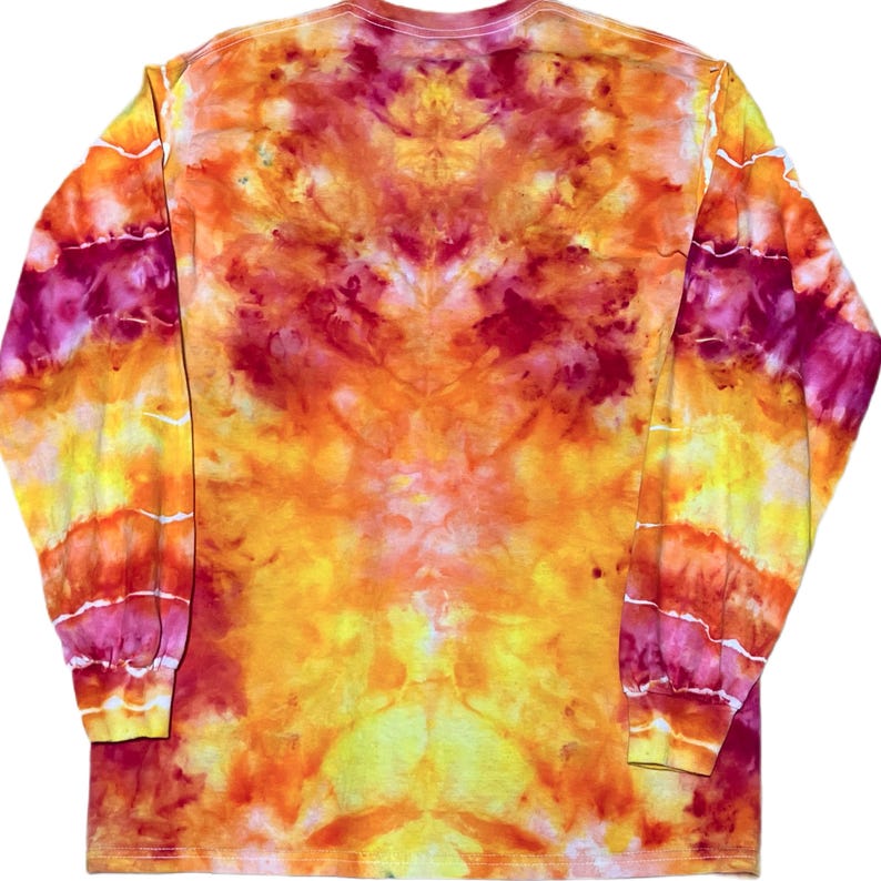 Puede incluir: Una camiseta de manga larga con un vibrante patr&oacute;n de te&ntilde;ido anudado en tonos naranja brillante, rojo intenso, magenta y amarillo soleado. El dise&ntilde;o muestra un efecto marmolado y arremolinado en toda la prenda, incluyendo las mangas y los pu&ntilde;os.