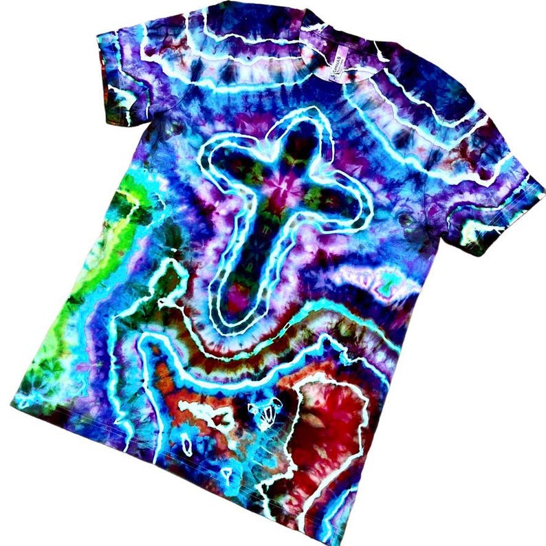 May include: A tie-dye t-shirt with a white cross design. The shirt displays a swirling pattern of blues, purples, greens, and reds. The short-sleeved tee is made of soft fabric.